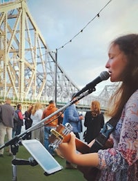 a woman singing in front of a microphone in front of a bridge