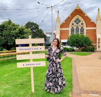 a woman standing next to a wooden sign in front of a church