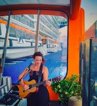 a woman playing an acoustic guitar in front of a cruise ship