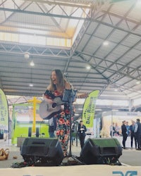 a woman playing an acoustic guitar at a trade show